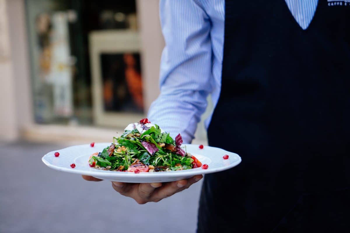 A hand presenting a fresh salad plate with mixed greens
