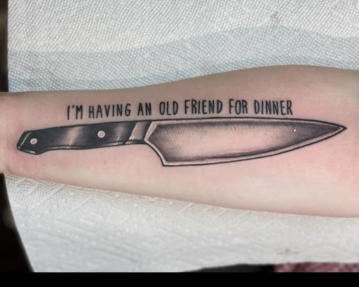 A tattoo of a knife with the text "I'm having an old friend for dinner".