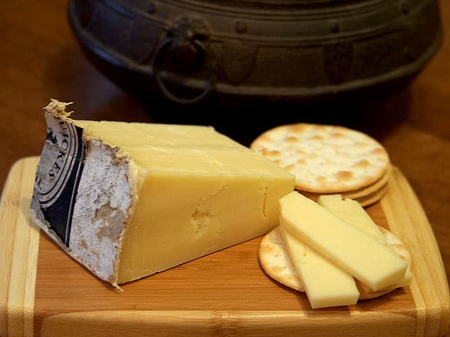 Piece of cheddar cheese on a wooden board.