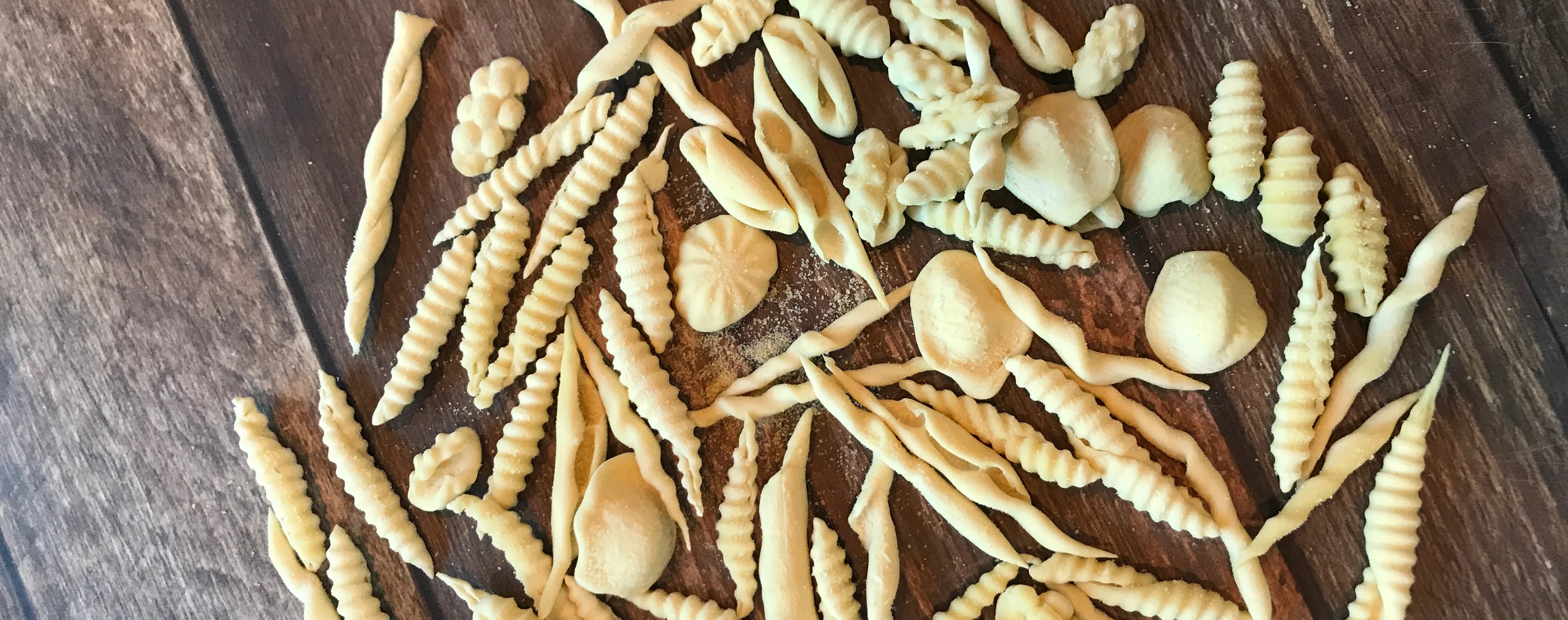 Assorted shapes of raw, hand-rolled pasta on parchment paper.