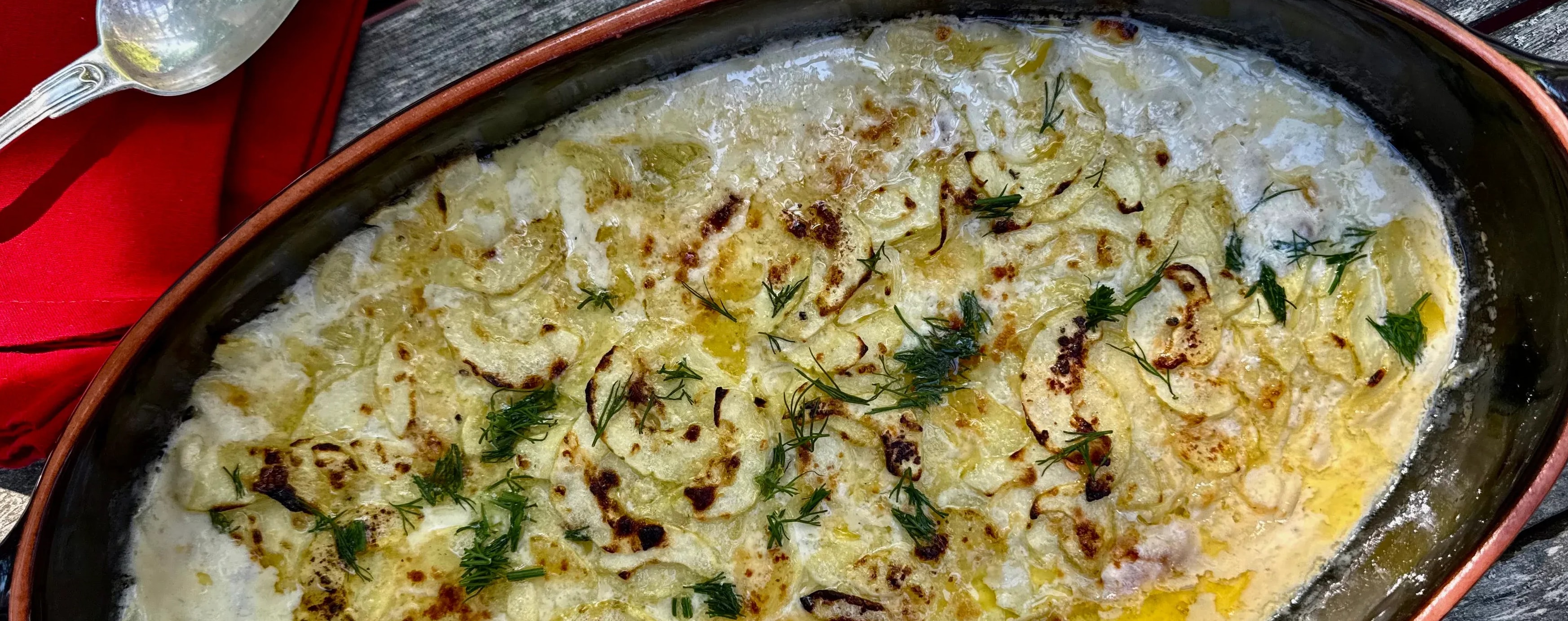 Hot cucumber gratin in a creamy sauce, in an oval ceramic dish on a gray wooden table.