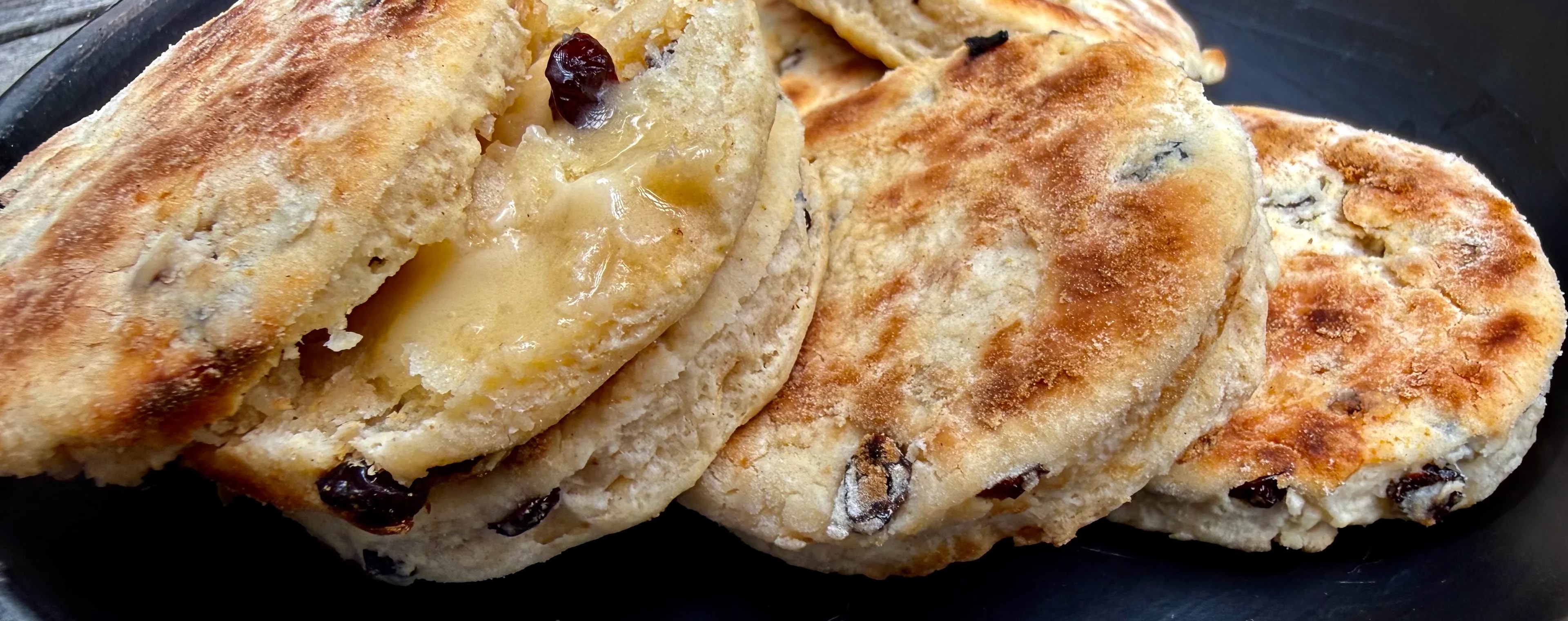 Griddle cakes, known as Singing Hinnies, rest on a black earthenware plate, ready to be eaten with butter and jam or other soft spread.