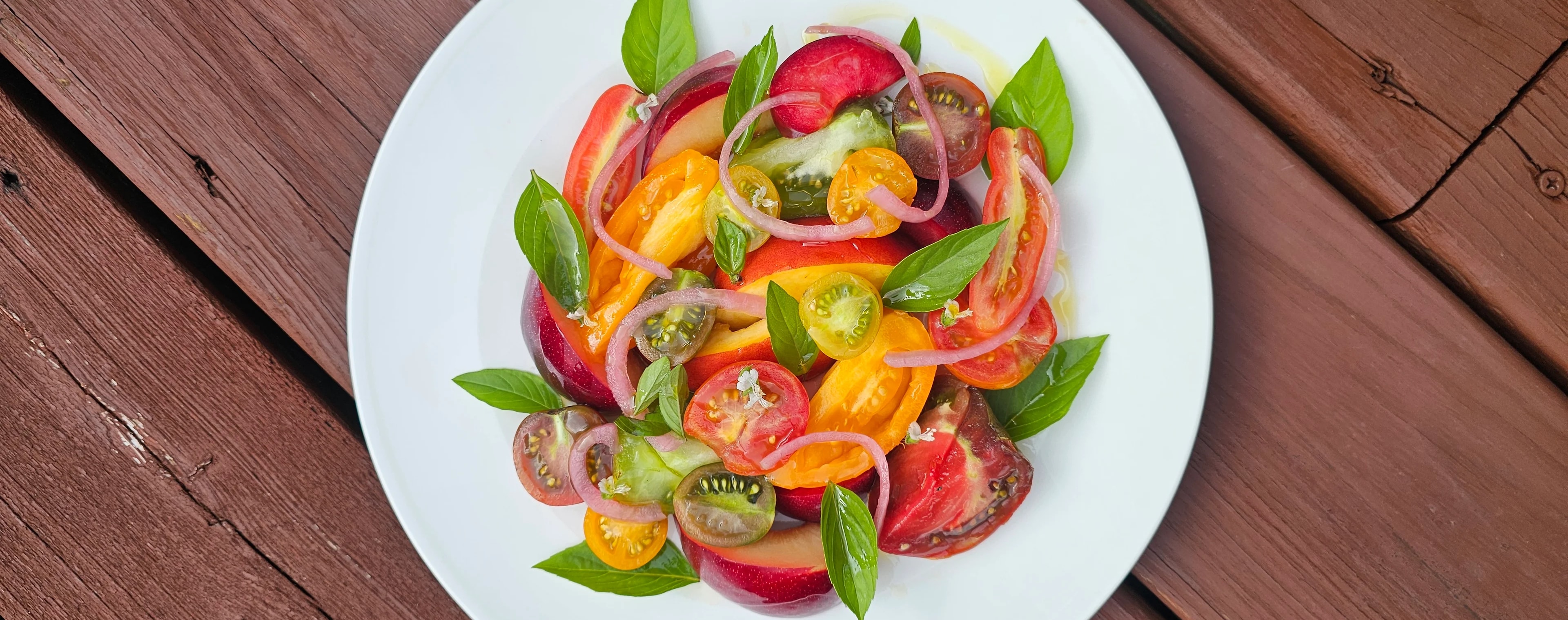 A vibrant compostion of peak-season heirloom tomatoes and juicy stone fruit, layered with fresh basil and pickled red onion to add acidity and texture.