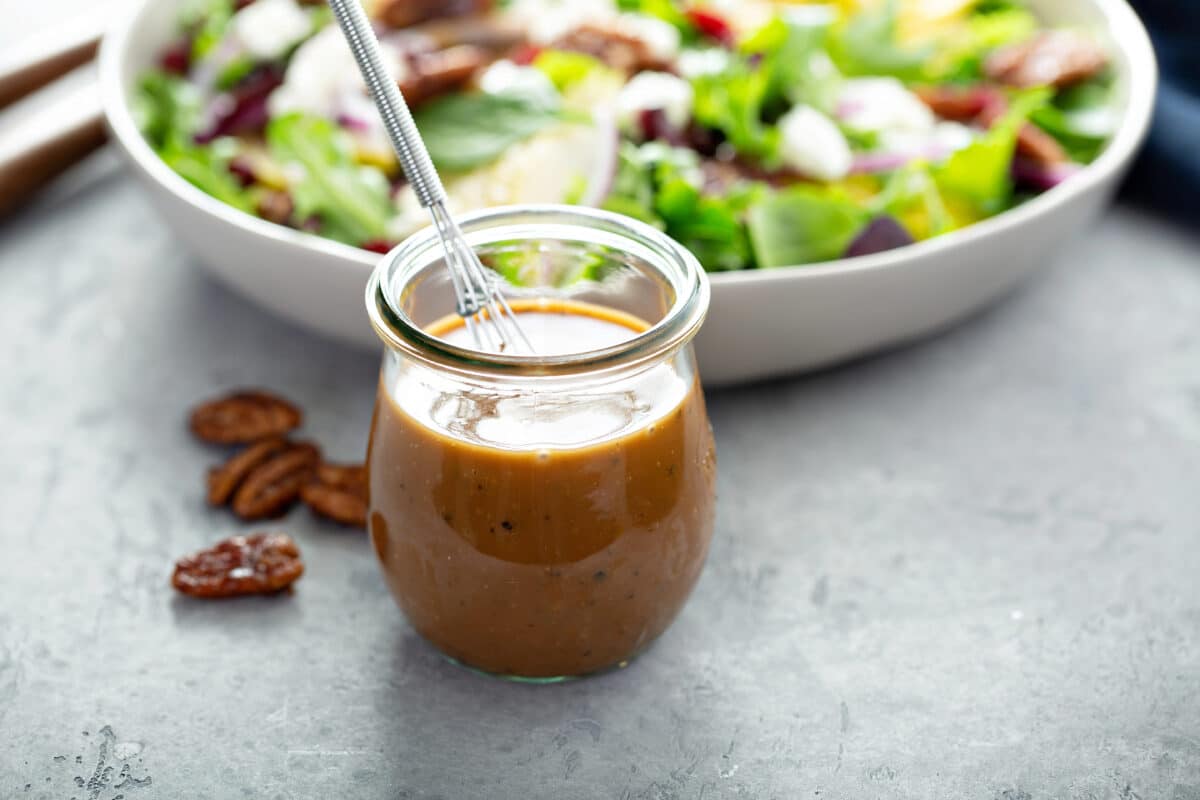 Opaque yellowish salad dressing in a small jar next to a green salad