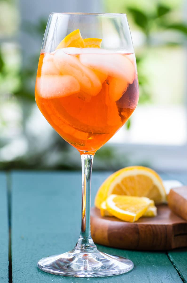 An Aperol Spritz cocktail with orange slices in a wine glass.