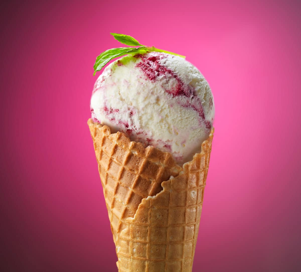 Ice cream cone with blackberry swirls and mint leaf on top.