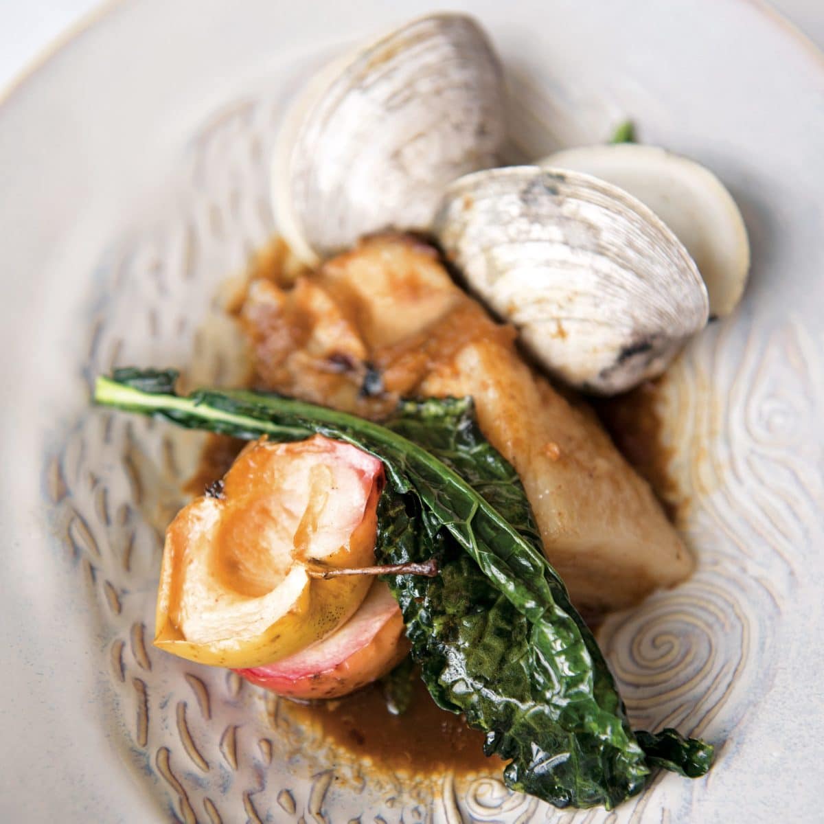A gourmet dish featuring clams, roasted meat, and greens.