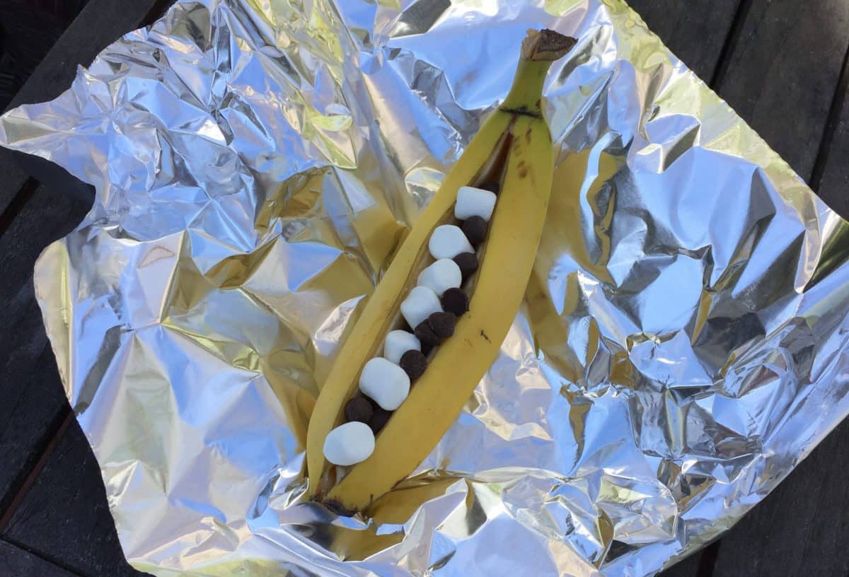 A sliced banana filled with chocolate chips and marshmallows, ready to be grilled.