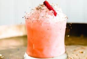 Close-up of Slippery When Wet cocktail topped with a frothy cream and a strawberry slice.